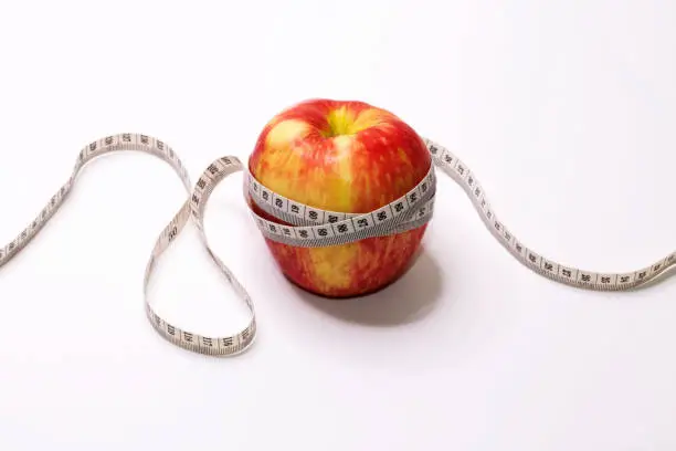 A tape measure wrapped around a red apple.
