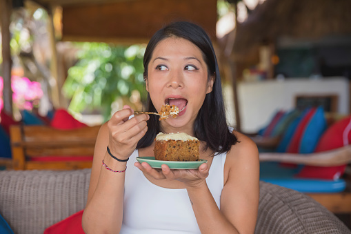 Portrait shot of a Malaysian female food blogger tasting a slice of carrot cake with cream cheese icing at a holiday villa.
