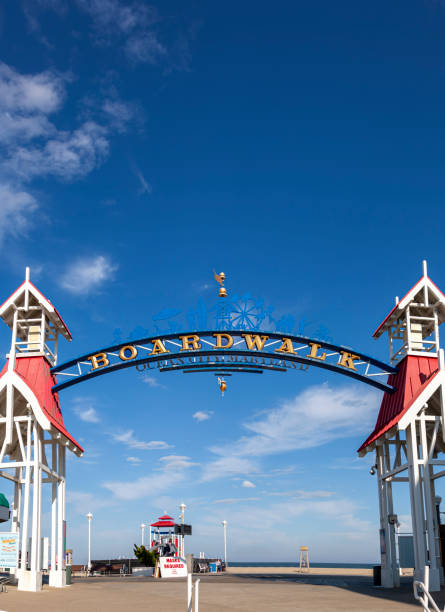 Image  of the entrance of famous board walk of Ocean City Image  of the entrance of famous board walk of Ocean City, MD by the beach where people are walking on a sunny afternoon. A popular tourist spot on east coast of USA. A wooden arch is erected to mark the spot. boardwalk stock pictures, royalty-free photos & images