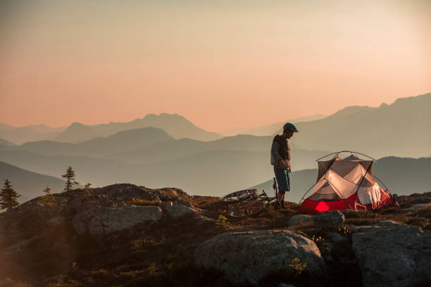 homme se préparant pour l’emballage de vélo dans des montagnes au lever du soleil. - tent camping lifestyles break photos et images de collection