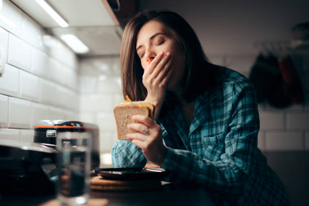 sleepy woman hält ein sandwich in der küche - eating sandwich emotional stress food stock-fotos und bilder