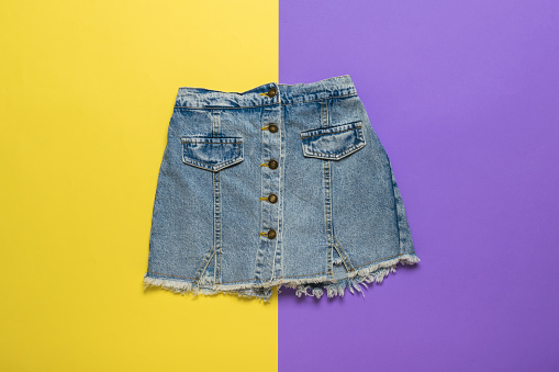 Short denim skirt on a background of yellow and purple flowers. Summer denim clothing.