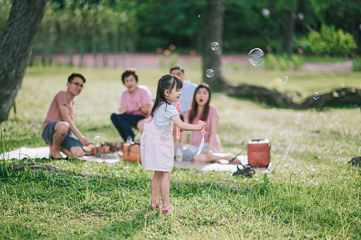 asian chinese daughter girl child with bubble wand at public park in the morning backlit sunlight