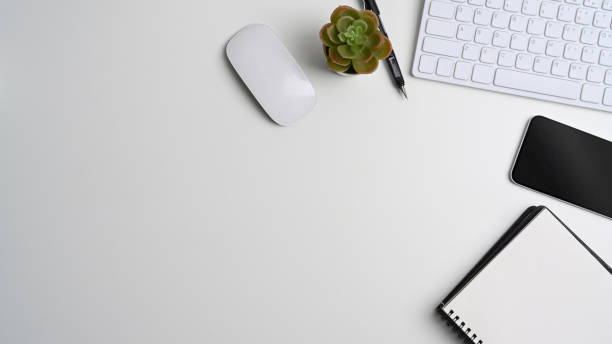 istock Above view of white office desk with empty notebook, smart phone, keyboard, cactus and copy space. 1314294882