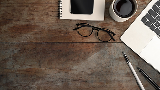 Above view of computer laptop, coffee cup, smart phone, eye glasses and notebook on wooden table.