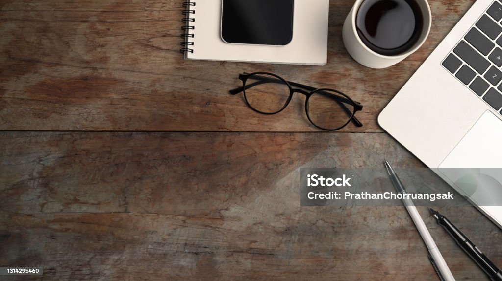 Above view of computer laptop, coffee cup, smart phone, eye glasses and notebook on wooden table. Desk Stock Photo