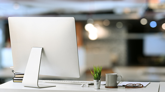 Modern workspace with computer, coffee cup, document and house plant on white desk in office interior.