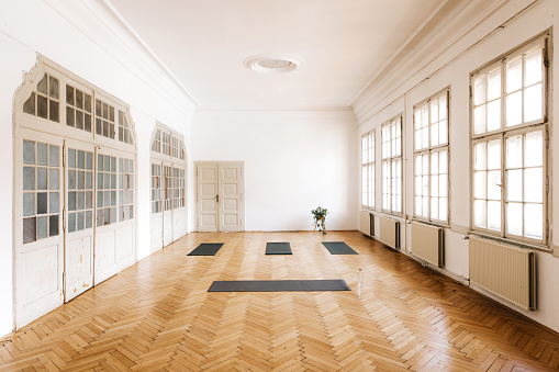 A photo from high angle of an empty spacious yoga studio with large windows. There are four rolled dark yoga mats. Horizontal daylight photo with copy space.