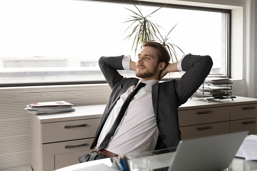 Satisfied businessman wearing suit stretching hands in office chair after work done, happy smiling executive manager leader boss leaning back, daydreaming, visualizing good future, new opportunities