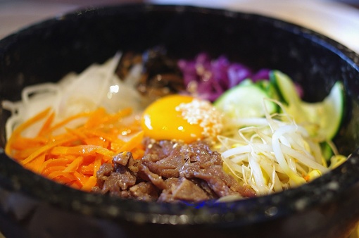 Dolsot (stone pot) bibimbap with raw egg yolk, carrots, beef (bulgogi), radish, onions, cabbage, zucchini, namul (root vegetables) and blanched bean sprouts at a Korean restaurant in Sydney, Australia.