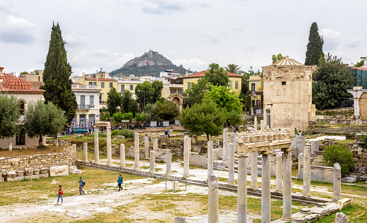 Athens – May 6, 2018: Tourists visit Roman Agora in Athens, Greece. Panorama of Ancient Greek ruins at Plaka district in Athens city center. Old Tower of Winds on right, famous landmark of Athens.