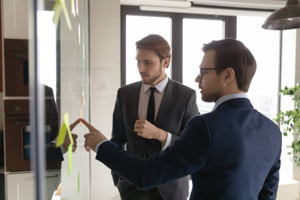 istock Confident businessman wearing glasses discussing sticky notes with colleague 1314317545