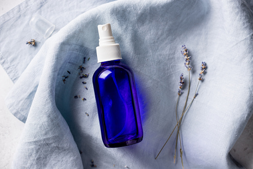 lavender spray in transparent glass bottle on linen sheet. Insomnia or depression treatment for sleepless nights. top view