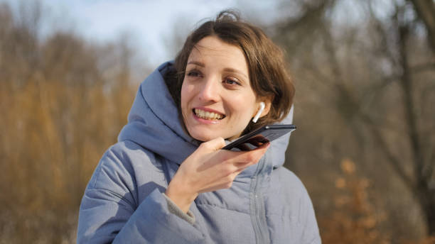 lady in blue coat sta inviando un messaggio vocale audio che spiega qualcosa sullo smartphone all'aperto parlando con l'assistente mobile. ragazza che usa il riconoscimento vocale e la dettatura dello smartphone - head in hands audio foto e immagini stock