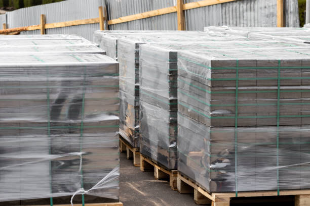 New film-wrapped building materials on pallets neatly stacked kerb paving stone and gray brick for the industrial street finishing of parks and streets of the city. High quality photo. nuevos materiales de construcción envueltos en película en palés cuidadosamente apilados de piedra de pavimentación de bordillos y ladrillo gris para el acabado de la calle industrial de parques y calles de la ciudad. foto de alta calidad
