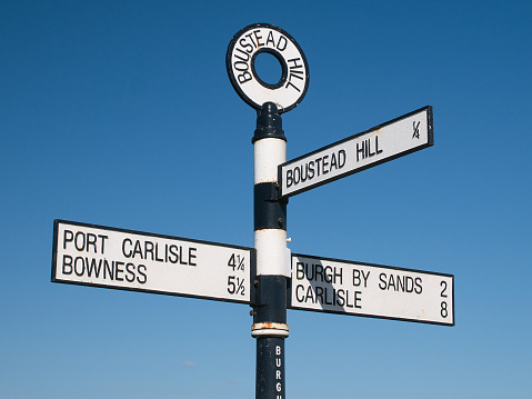 Boustead Hill, UK - Apr 15 2021: A metal, black and white signpost at Boustead Hill on the Solway Coast, Cumbria, UK. The sign is on the Hadrians Wall Path route. Taken on a cloudless sunny day.