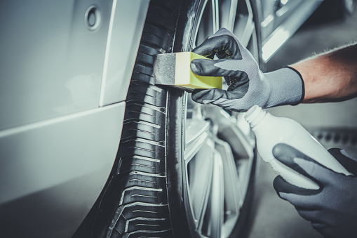 Caucasian Car Detailing Worker Taking Care of Modern Vehicle Tires and Alloy Wheels. Vehicle Detail Cleaning. Automotive Industry Theme.