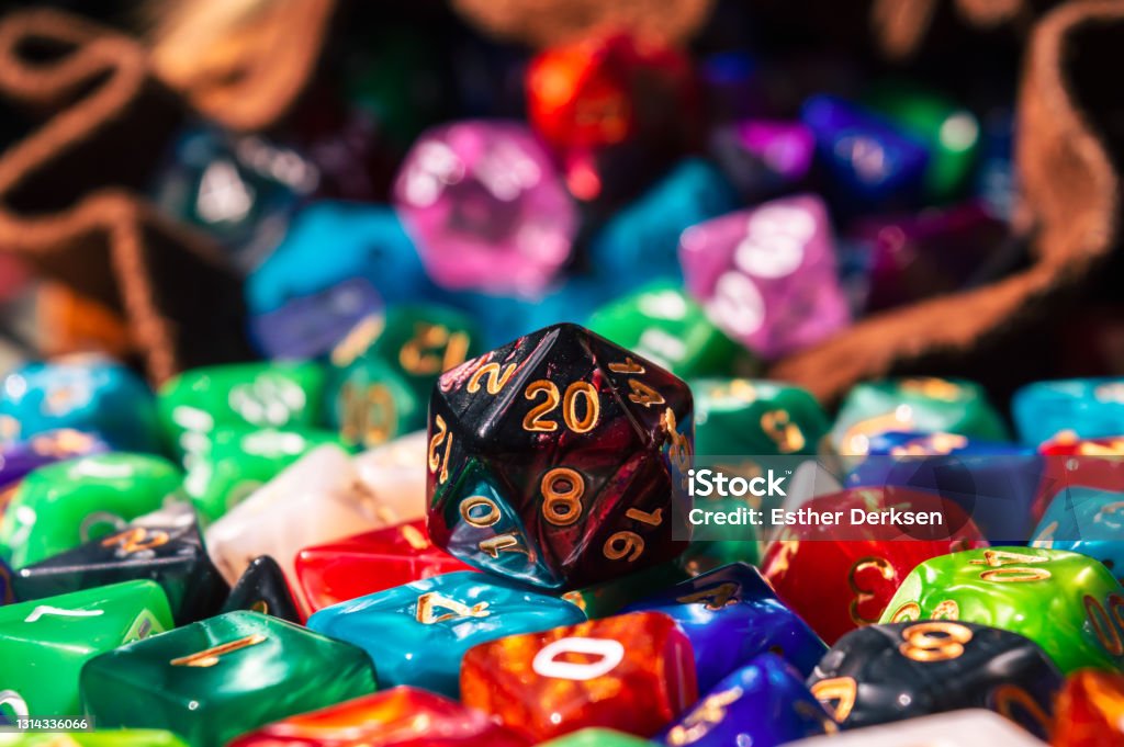 Close-up of a d20 on a pile of dice Close-up image of a black and red marbled 20-sided die on a pile of various colored and shaped dice spilling out of a dice bag in the warm sunlight Dice Stock Photo