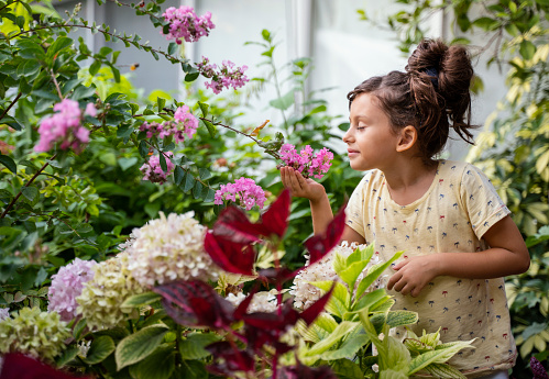 Cute little girl with a hair bun smelling flowers in a spring garden