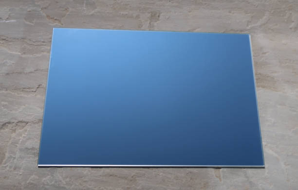 Plain sheet of mirror glass reflecting blue sky lying on a light grey slate