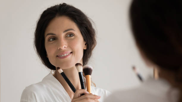 istock Close up smiling woman holding cosmetics brushes, looking in mirror 1314340517