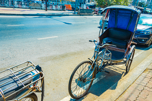 A local driver waits for passengers in his tuk-tuk on a city street in downtown Hanoi, Vietnam