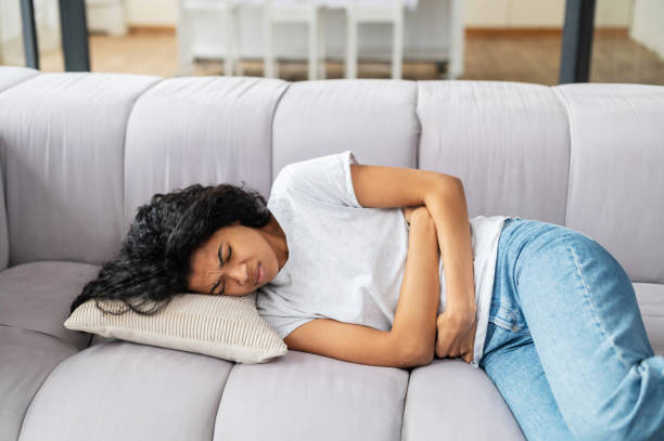 istock Young multiethnic woman is lying on a sofa and suffering from stomach ache 1314348827