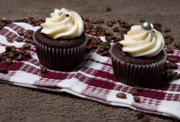 two homemade cupcakes and coffee beans on brown cloth background, homemade cake with cream