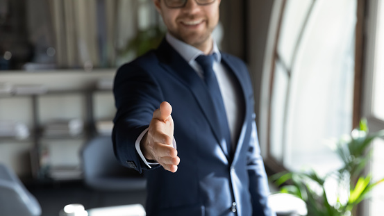 Close up cropped portrait of smiling successful friendly young man in formal attire hr recruiter stretching hand to camera glad to offer you job in company, greeting spectator as new workforce member