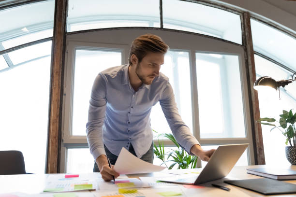 istock Concentrated male project manager standing by desk involved in paperwork 1314352282