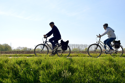 Wilsele, Vlaams-Brabant, Belgium - April 25, 2021: bright sunny Sunday. Caucasian adults enjoying a beautiful weekend activity like walking or riding bike along a farmland on a bicycle walking lane track.