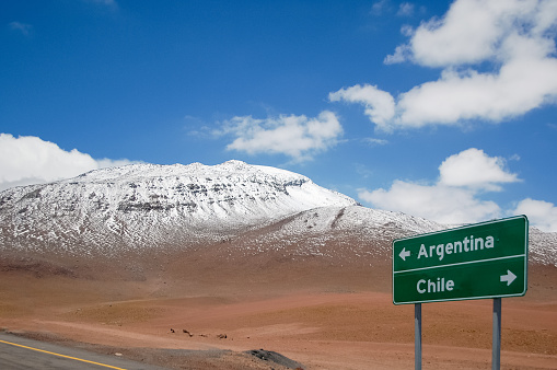 Highway sign with directions for Argentina and Chile at the border. Road sign in with mountain range and snow in the background. Road trip and adventure concept in South America.