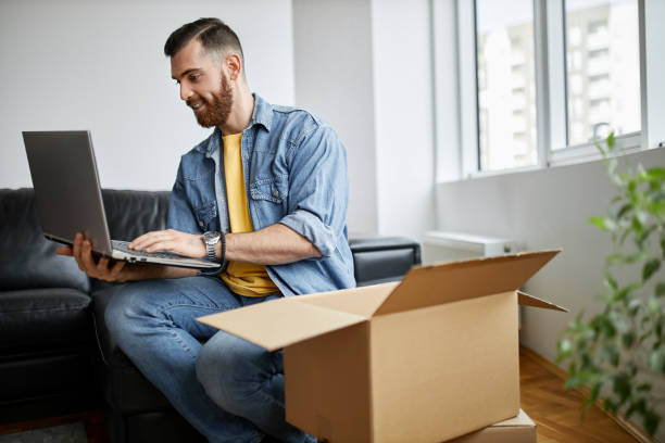 istock Man using his laptop, sitting on the floor surrounded by moving boxes. 1314358113