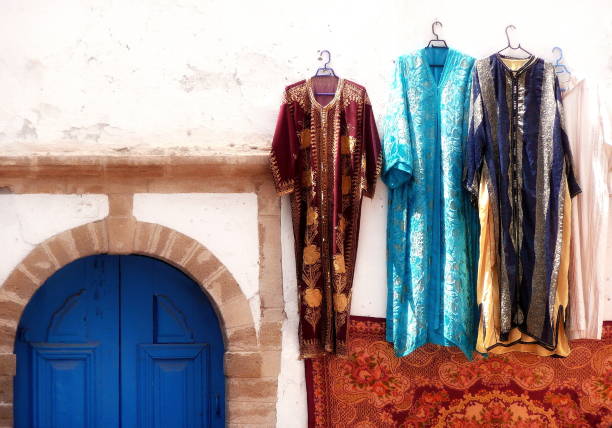 Smiling Moroccan man in vibrant traditional attire stands in front of a blue shop in Essaouira. His colorful outfit and joyful expression highlight Moroccan culture, heritage, and local street life.