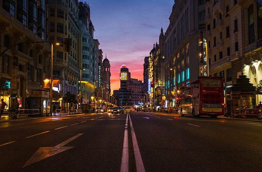 Low-angle view of Madrid's busy Gran Vía street at dusk, with Callao and the Edificio Carrion with the Schweppes sign glowing in the bakcground.
