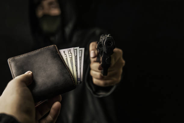 Man's hand holds out purse of money to robber with gun. Armed robbery. Man's hand holds out purse of money to robber with gun. Firearm is pointed at camera. Criminal in hood and mask. Assault on unarmed man. Hundred and fifty dollars in open wallet. wallet gun stock pictures, royalty-free photos & images