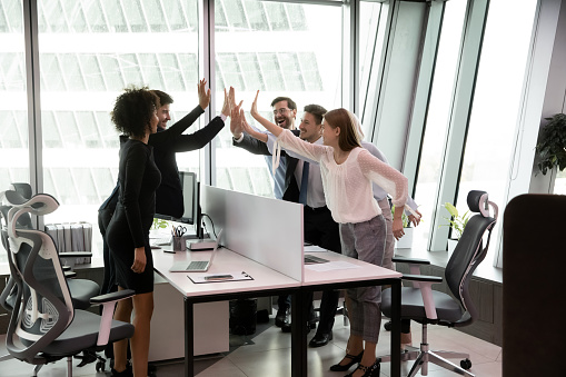 Overjoyed diverse multiracial businesspeople give high five engaged in teambuilding activity in office. Happy excited multiethnic colleagues employees celebrate shared team success or achievement.