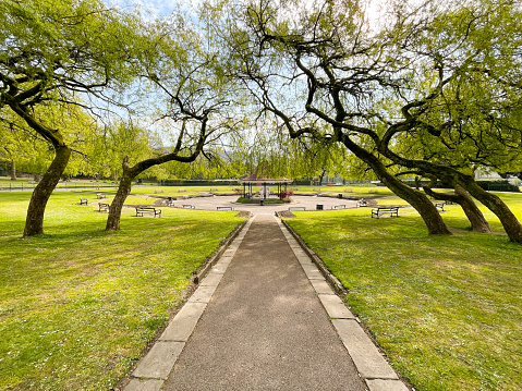 Pontypridd, Wales - April 2021: Footpath leading to the bandstand in Ynysangharad Park with the view framed by leaning trees