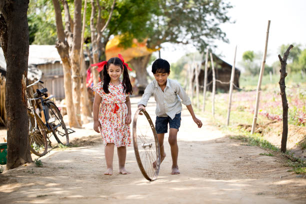 Children rolling tyre wheel on village road Rural boy and girl playing with tyre wheel on road indian boy barefoot stock pictures, royalty-free photos & images