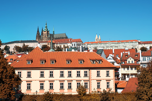 Prague travel view with Castle, St. Vitus Cathedral and red roofs of historic residential buildings. Autumn cityscape with skyline. Orange, blue colors. European travel cityscape