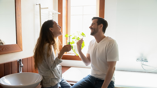 Smiling young multiethnic man and woman newlyweds brush teeth in cozy bathroom in new home or apartment. Happy millennial couple renters enjoy morning together wash clean in bath. Rent concept.