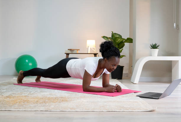 istock Mid adult African woman performing home workout, She is watching online tutorial on laptop 1314382583