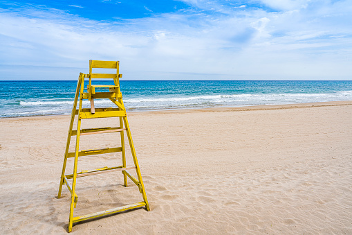Yellow lifeguard chair on empty sand beach with blue sky. Copy space. High resolution 42Mp outdoors digital capture taken with SONY A7rII and Zeiss Batis 25mm F2.0 lens