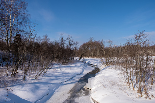 Winter landscape with a small snow-covered river on a sunny day, Russia.