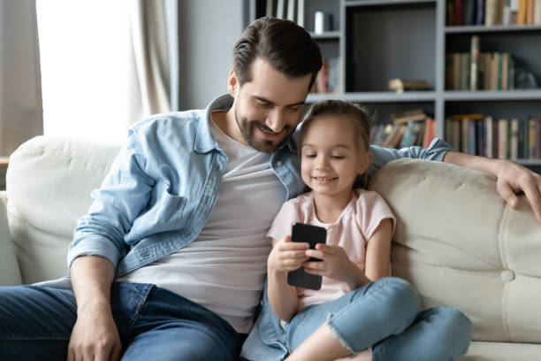 istock Happy young dad watching small daughter playing game on smartphone. 1314393264