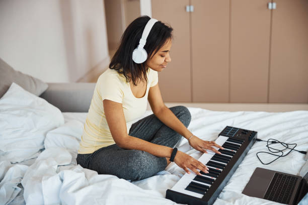 istock Charming young woman playing synthesizer and using laptop at home 1314394821