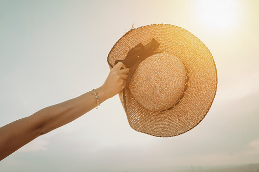 hand holding a straw hat and sky