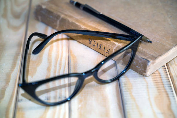 very old physics book on a wooden table with a reading glasses and a pencil for taking notes.