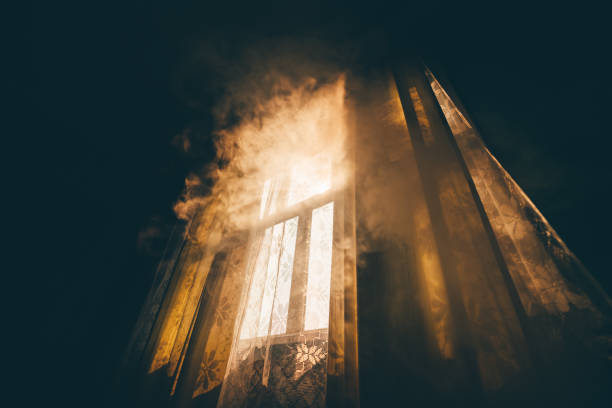 A mysterious smoke-shrouded window A wide-angle mysterious view from a dark room on a smoke-shrouded window lit by morning or evening sun illuminating the smoke with warm light and casting shadows on the tulle and curtains haunted house stock pictures, royalty-free photos & images