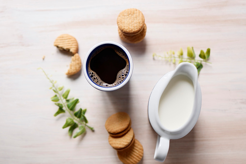 Istanbul, Turkey-April 25, 2021: A blue ceramic coffee mug with drip coffee, a creamer, green leaves and biscuits on a beige light brown wooden background. Shot with Canon EOS R5.